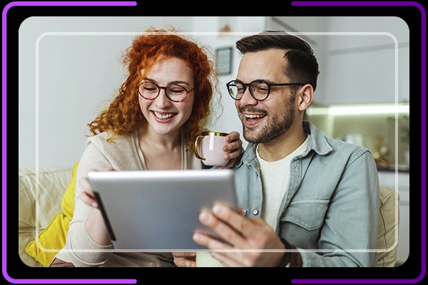 Imagem de casal, uma pessoa está segurando uma xícara e outra um tablet, as duas estão sorrindo