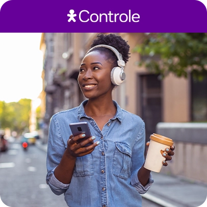 Imagem de mulher com fone de ouvido, segurando celular em uma mão e um copo de café em outra