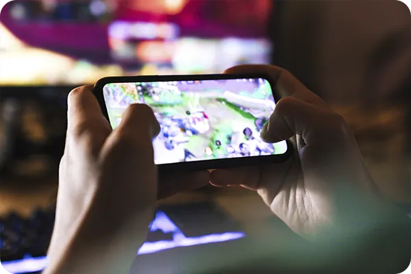 Mãos segurando celular durante partida de jogo móvel em ambiente interno.