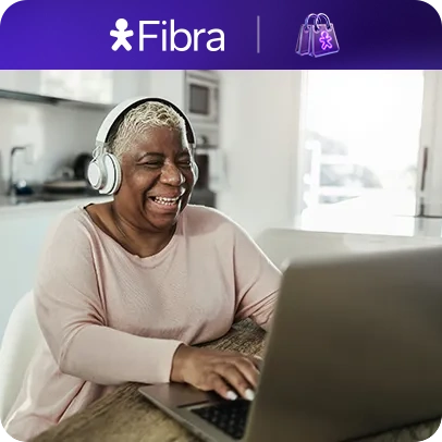 Mulher com fones de ouvido usando notebook em uma cozinha com logo Vivo Fibra e sacolinha no topo.