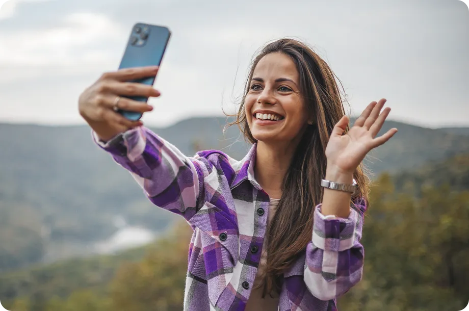Mulher com camisa xadrez fazendo vídeo chamada, ao fundo paisagem de natureza.