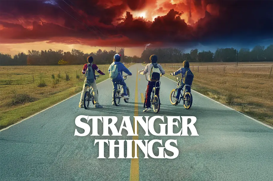 Imagem dos 4 personagens principais de Stranger Things em bicicletas, ao fundo céu avermelhado.