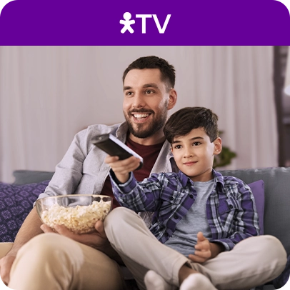 Pai e filho assistindo TV com pipoca e controle remoto em mãos.