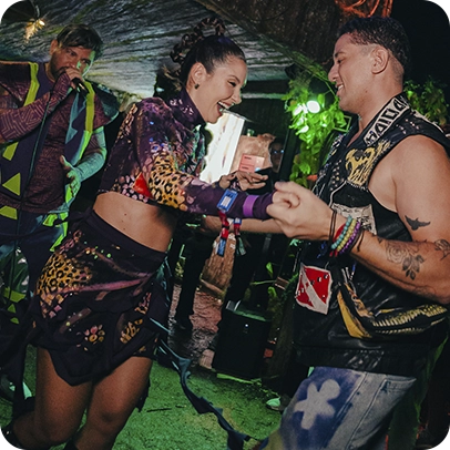 Festa com pessoas dançando, roupas coloridas e luzes ao fundo.