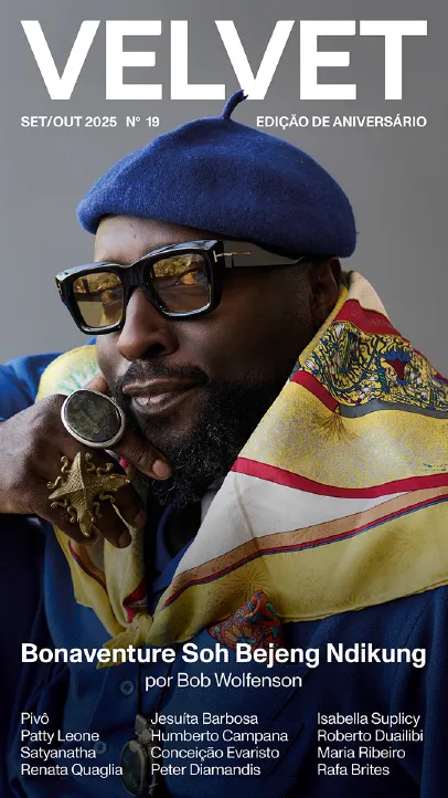 Imagem de um homem com uma boina azul, óculos, anéis e um lenço no pescoço