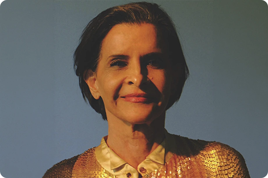 Marina Lima sorrindo, vestindo camisa de lantejoulas laranja.