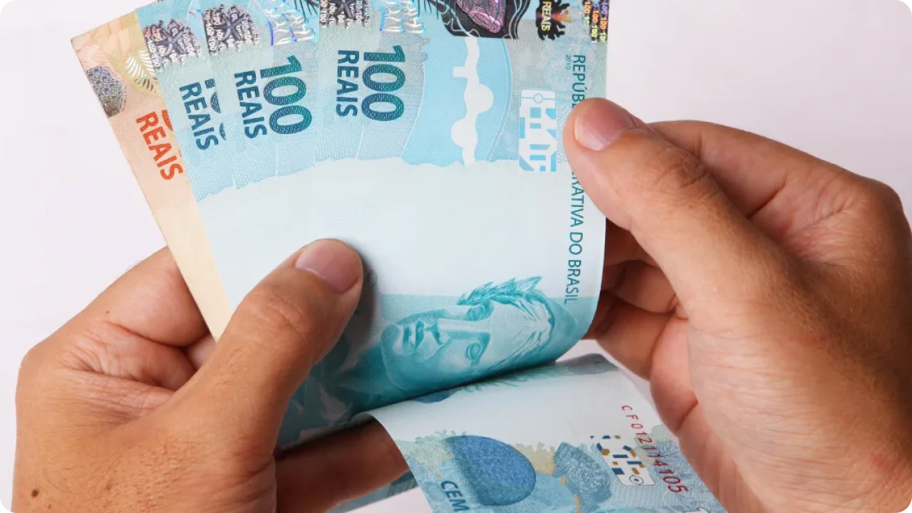 Mão de uma pessoa contando notas de 100 e 50 reais.