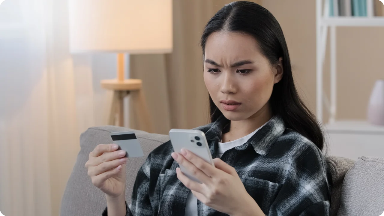 Mulher asiática analisando compra online enquanto segura o cartão de crédito.