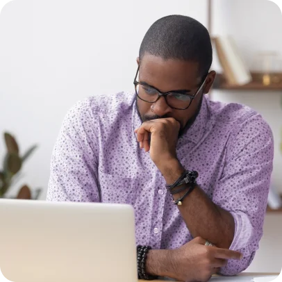 Homem negro pensativo apoiando o queixo na mão enquanto usa o notebook.