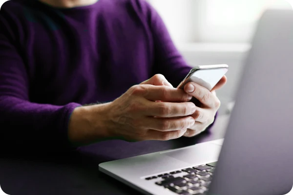 Pessoa utiliza smartphone ao lado de notebook para acessar dados digitais.
