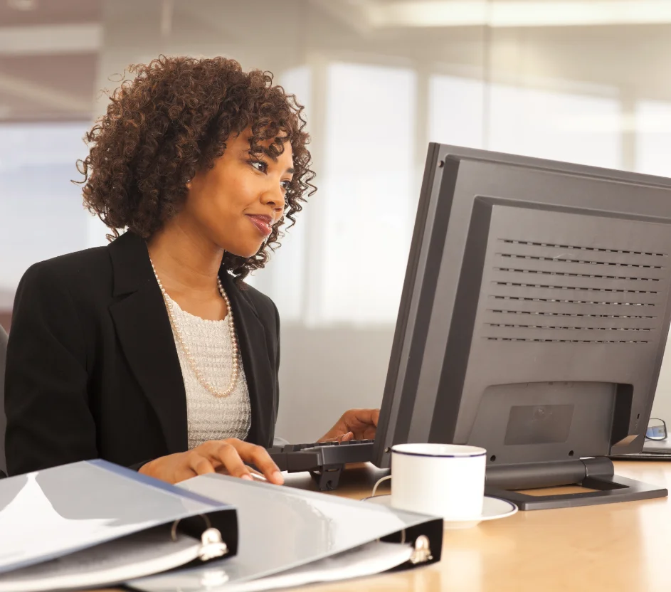 Mulher negra usando trabalhando em um computador com pastas ao lado