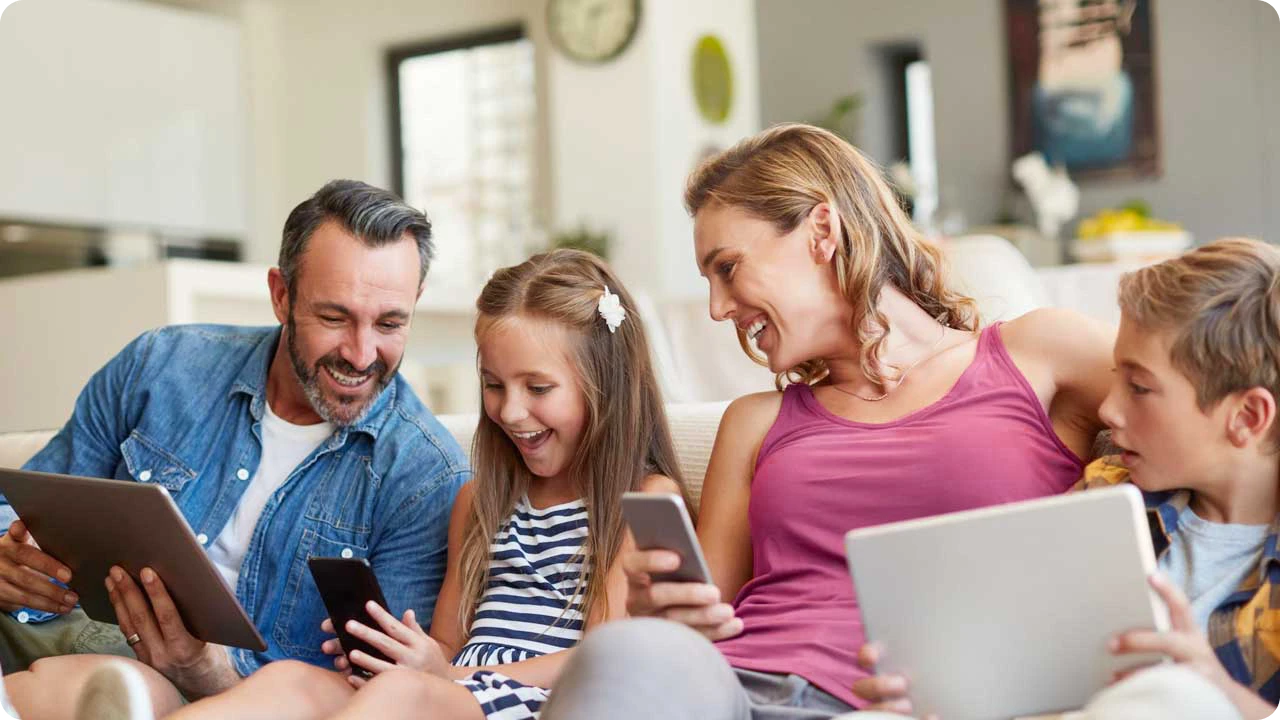 Pessoas reunidas no sofá usam diferentes dispositivos conectados.