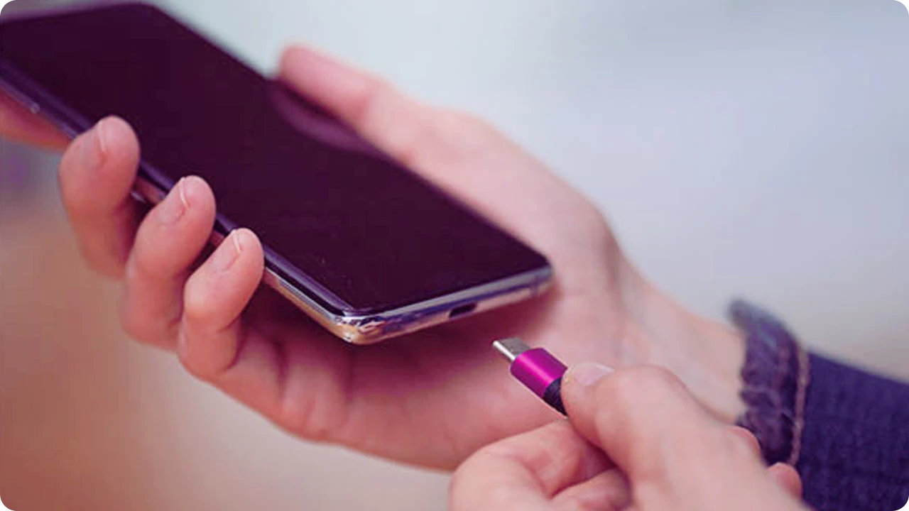 Mãos seguram celular enquanto aproximam conector de carregamento.
