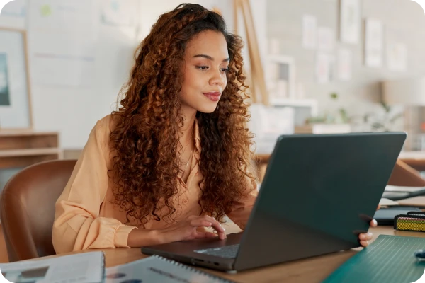 Pessoa trabalha em notebook em ambiente interno com itens de escritório.