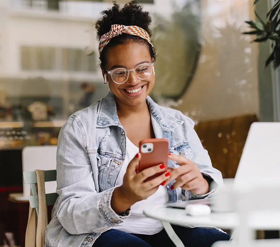 Mulher negra sorridente usando óculo e lenço no cabelo usando o celular