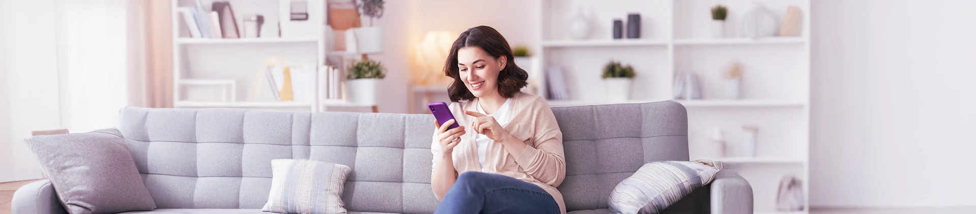 Mulher mexendo no celular sentada em um sofá na sala de uma casa.