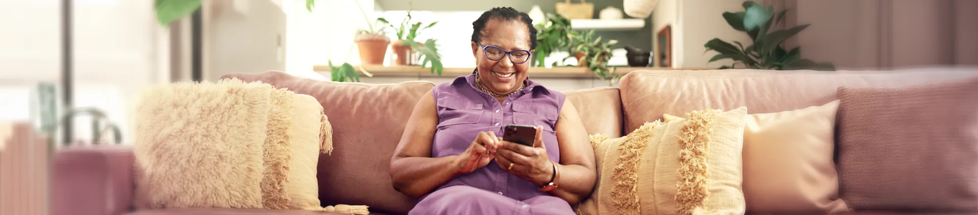 Senhora sentada em um sofá utilizando o smartphone.