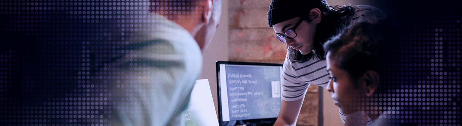 Foto de três pessoas concentradas olhando a tela de um computador.