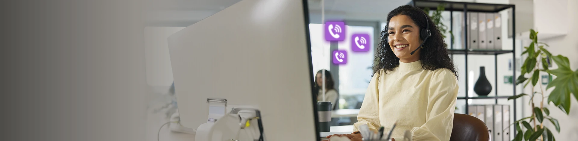 Imagem de uma mulher sentada em frente ao computador, com fones de ouvindo recebendo ligações