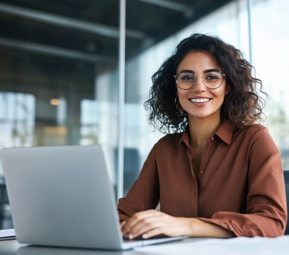 Mulher sorridente usando óculos de cabelos ondulados trabalhando no notebook