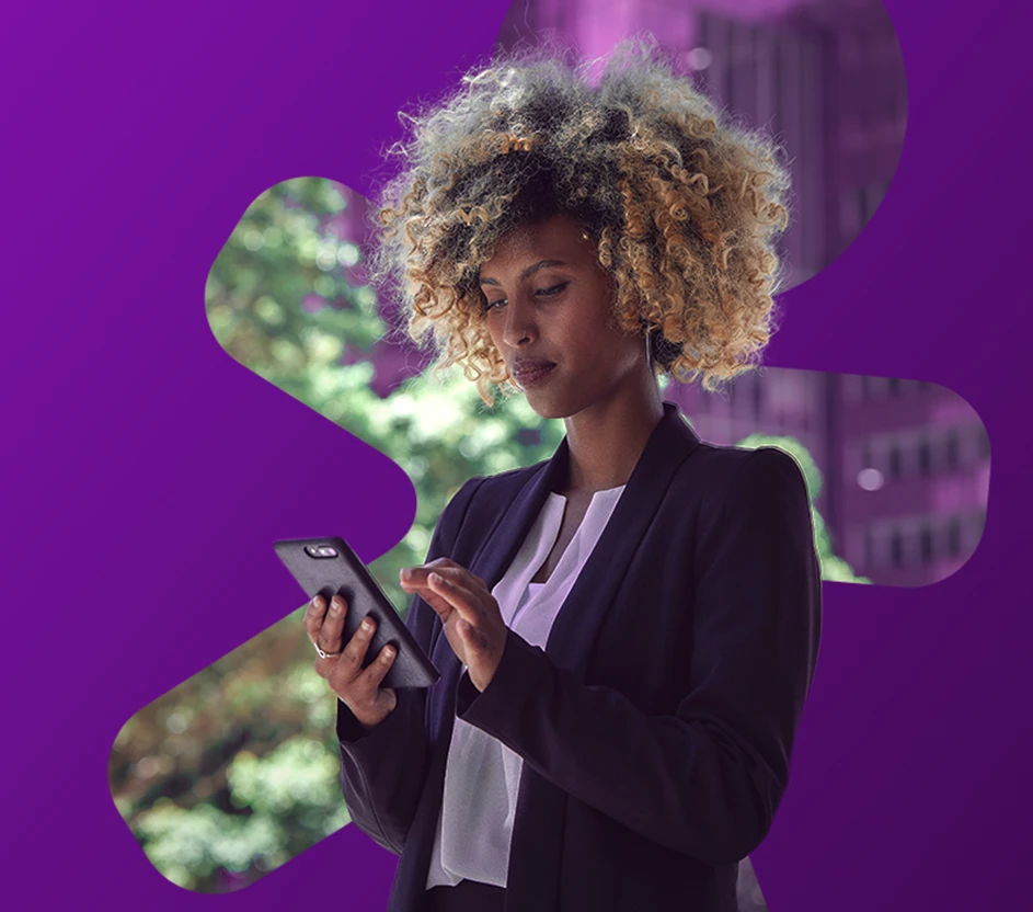 Mulher com cabelo encaracolado loiro usando celular na mão do lado de fora de um prédio com árvores.