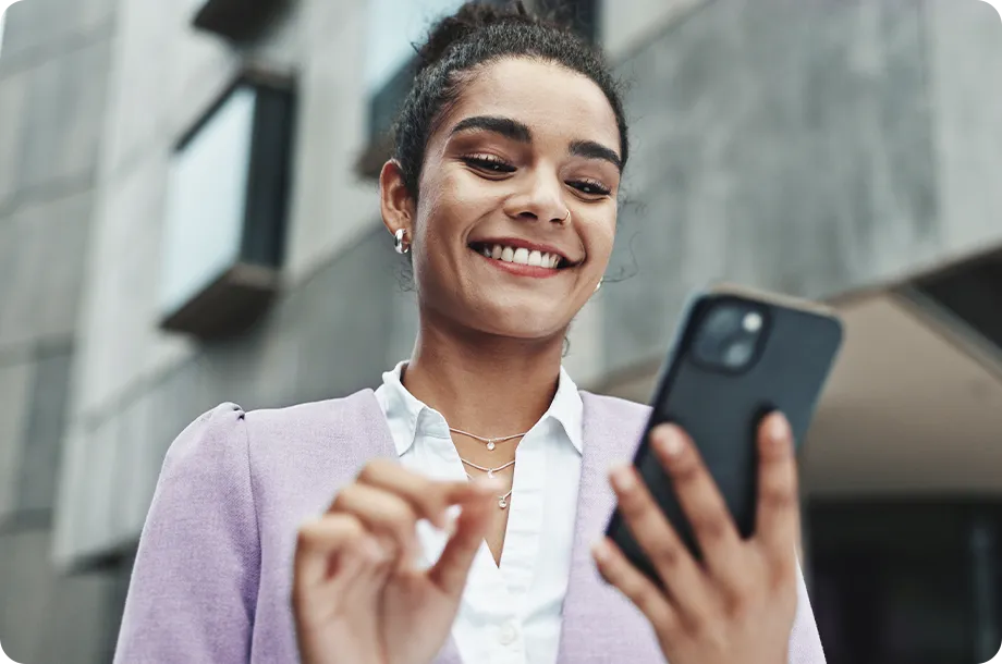 Mulher com terno roxo, segurando celular e sorrindo.