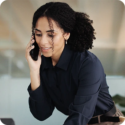 Mulher com cabelo cacheado, vestindo camisa preta e falando ao celular.
