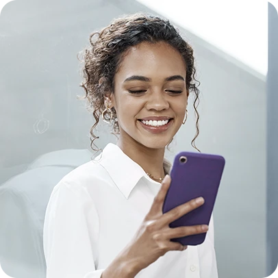 Mulher vestindo camisa branca, segurando celular e sorrindo.