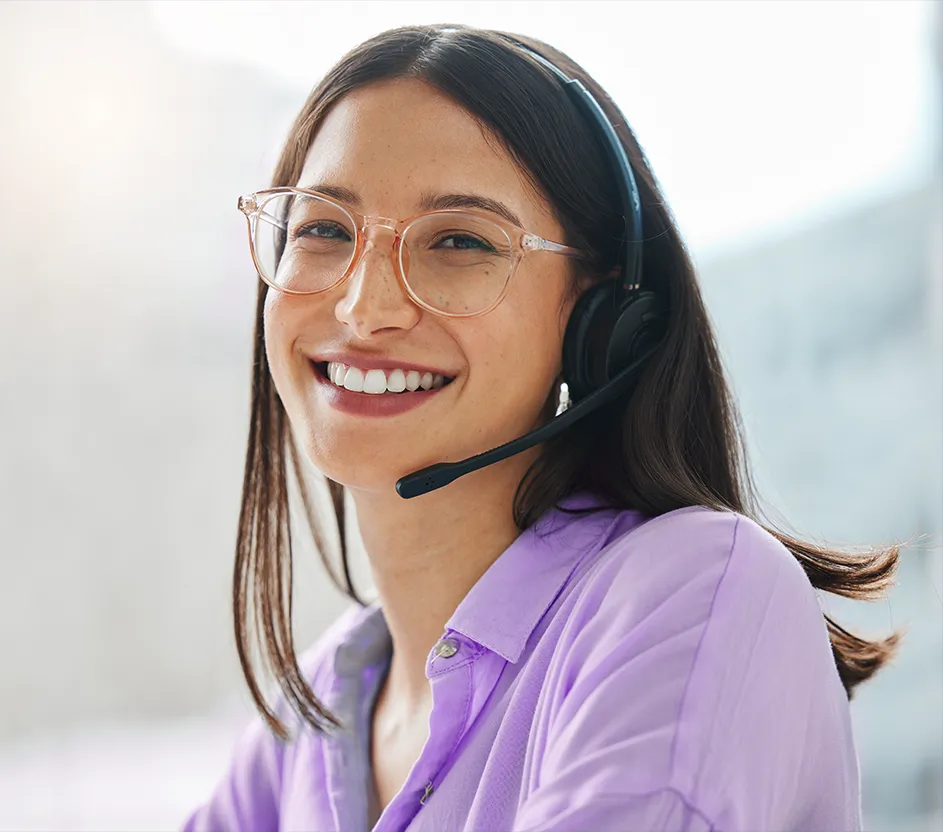 Mulher sorrindo, usando óculos de grau e headset na cabeça, com camisa cor púrpura.