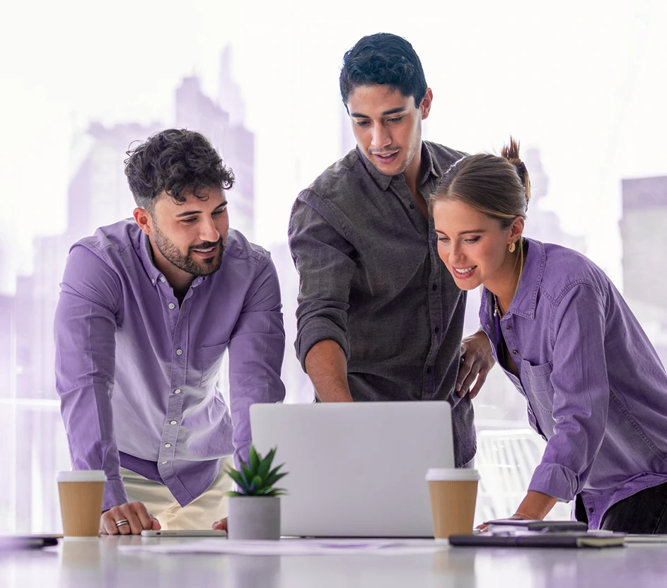 Foto de dois homens e uma mulher, discutindo em frente olhando para um notebook em um escritótio.