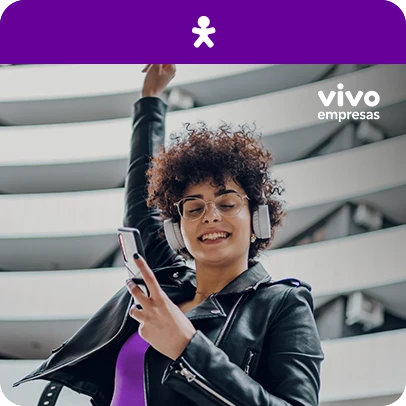 Mulher de jaqueta preta e fones, segurando celular. Acima logo da Vivo e Vivo empresas