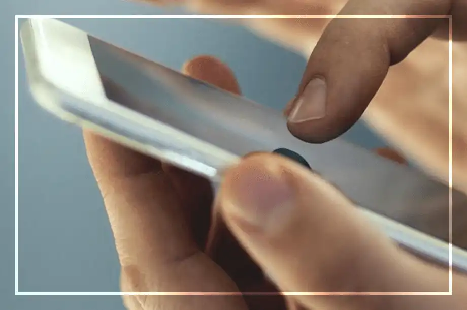 Mão segurando um smartphone enquanto o dedo toca a tela. Fundo desfocado.