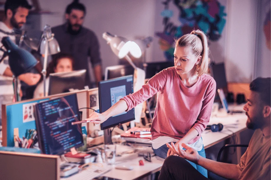 Ambiente de trabalho com pessoas trabalhando em destaque uma mulher apontando para um computador.
