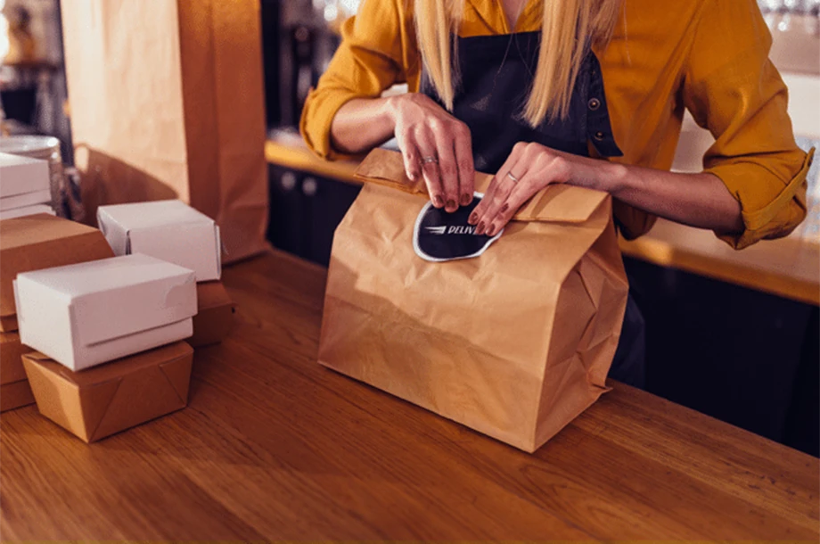 Mulher fechando sacola de delivery em restaurante.
