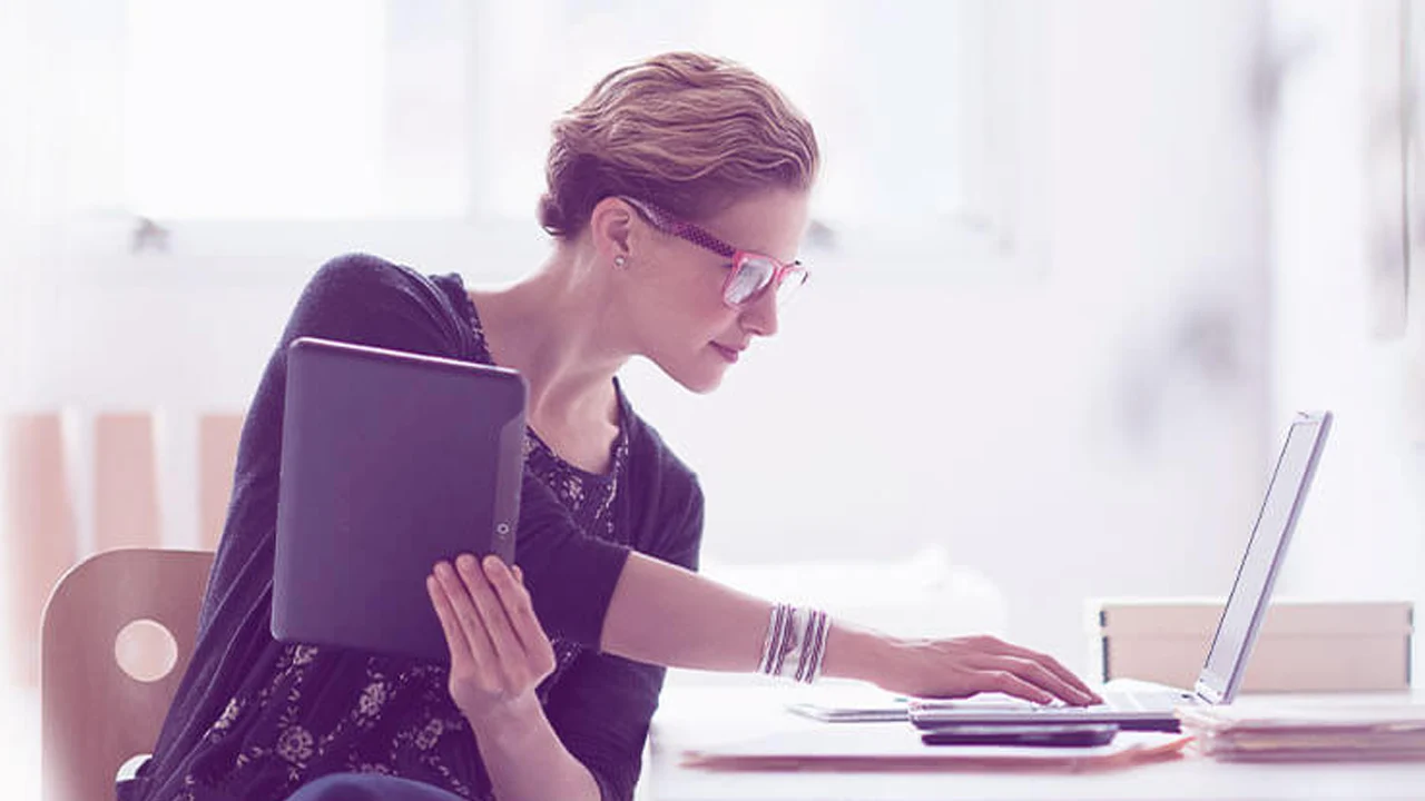 Pessoa usando tablet e notebook em ambiente claro com fundo desfocado.