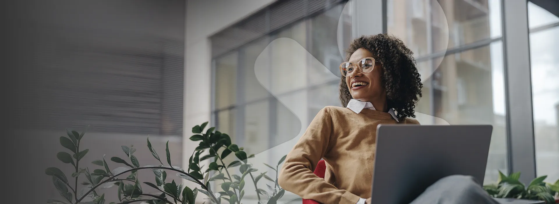 Pessoa com notebook em espaço corporativo com plantas e grandes janelas.