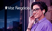 Mulher sorrindo com celular na mão e usando fones de ouvido com logo Vivo Voz Negócio em cima.