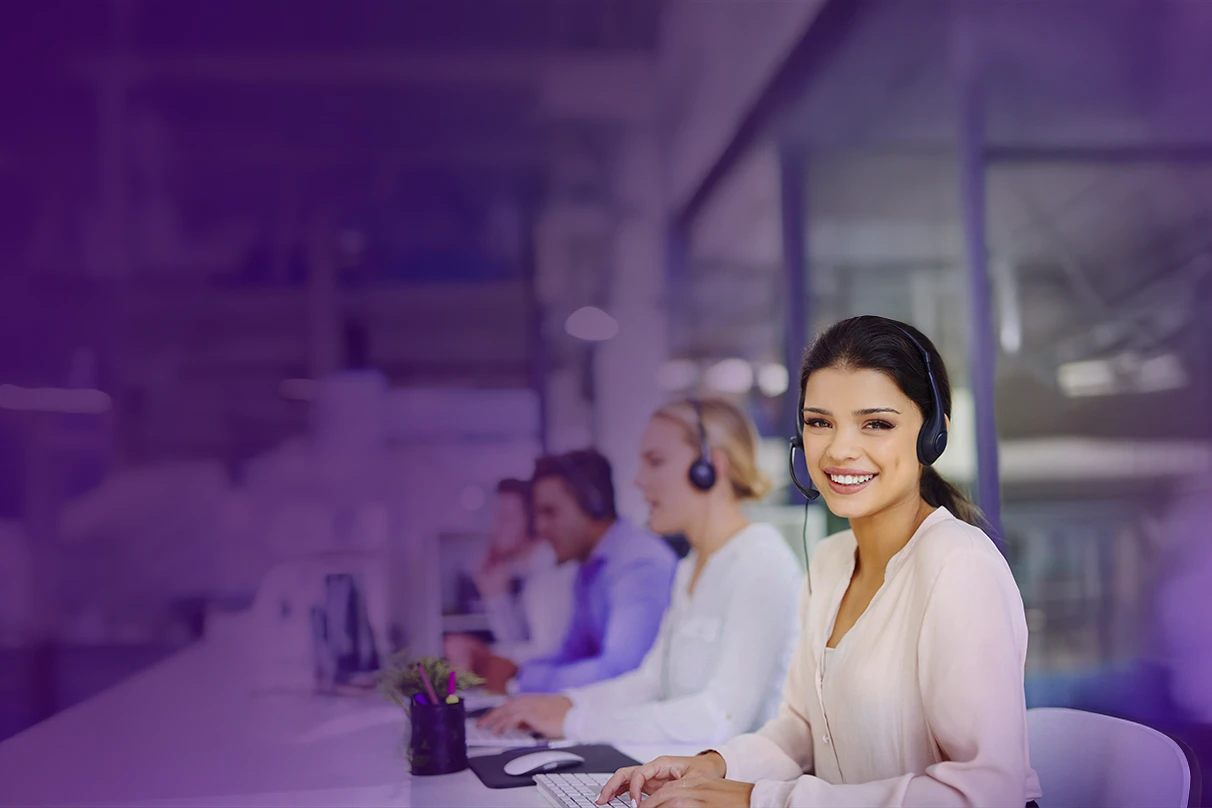 Mesa com vários atendentes com fone no ouvido e mulher em destaque sorrindo.